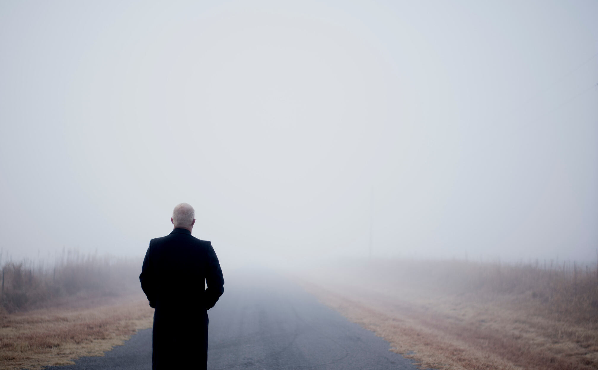 A Back View of a Man Standing on a Foggy Road